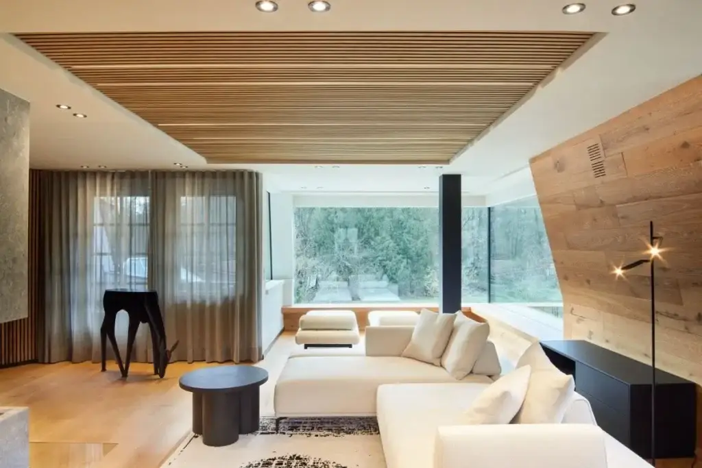 Wohnbereich mit weißem Ecksofa, Holzlamellendecke und großer Fensterfront in der Private Wellness Suite