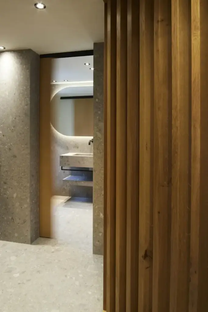 Blick an Holzlamellen vorbei ins Bad mit Steinwaschtisch in der Private Wellness Suite