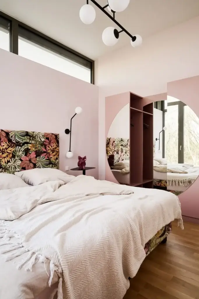 Schlafzimmer mit floral bezogenem Bett, rosa Wänden und Rundspiegel in der Ferienwohnung