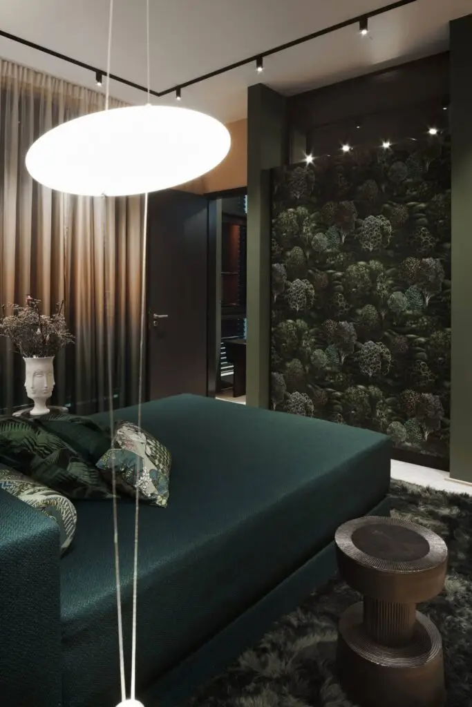 Schlafbereich mit dunkelgrünem Bett, Blätter-Tapete und Pendelleuchte im Business Apartment
