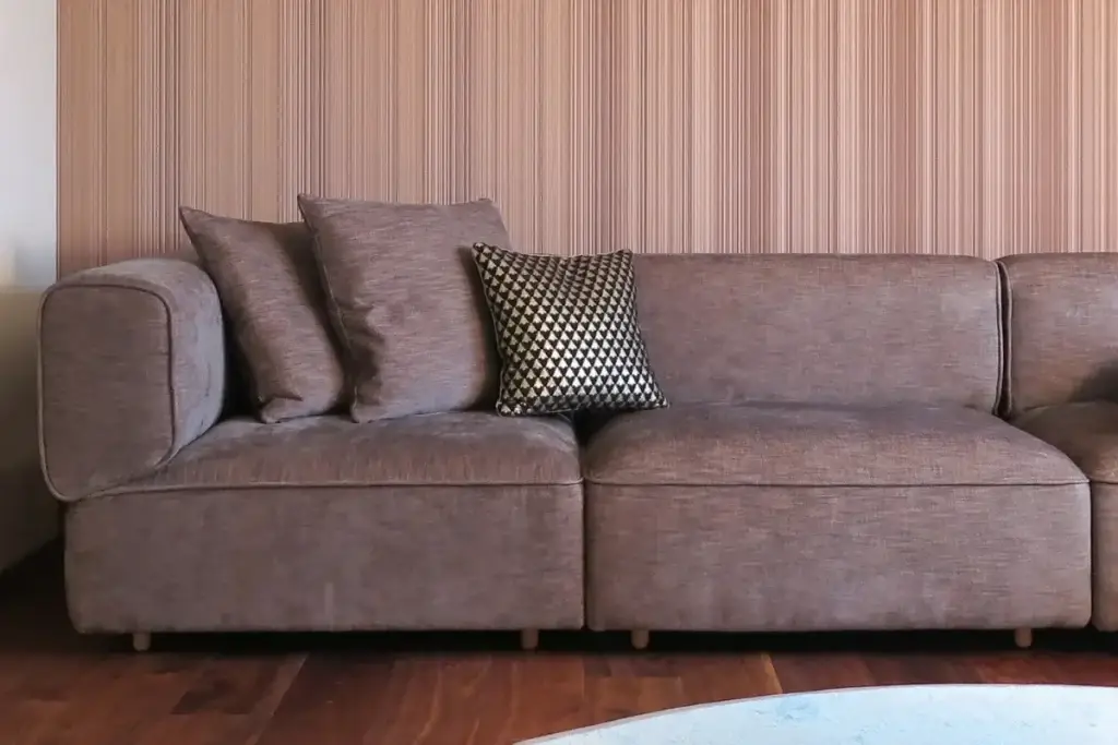 Taupefarbenes Sofa mit Kissen vor feingestreifter Wandtapete im Haus S