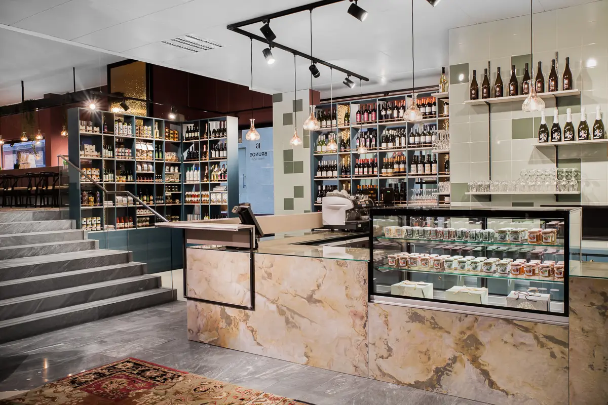 Theke mit Echtsteinfurnier und Vitrine in Bruno's Finest Food, dahinter petrolfarbene Weinregale