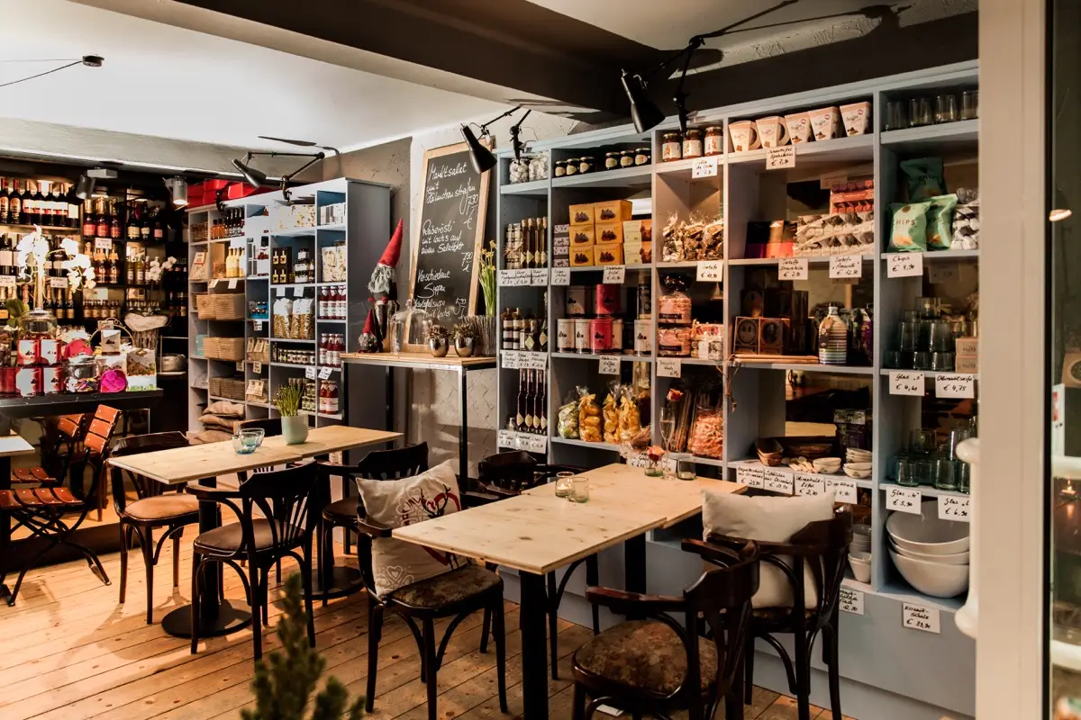 Feinkostgeschäft mit schwarzen Regalen voller Delikatessen und Bistrotischen