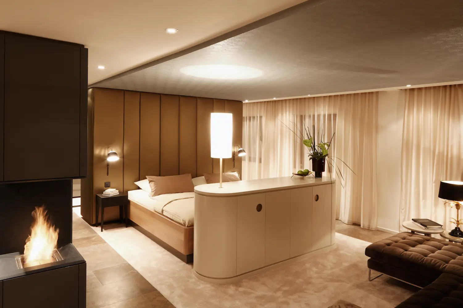 Hotelsuite mit Bett vor raumhoher Polsterwand, halbrundem Sideboard und Kamin