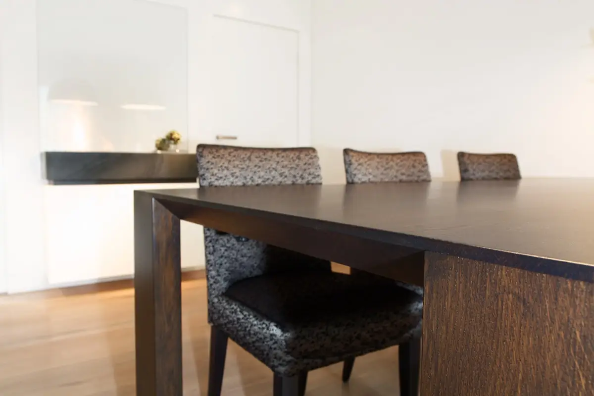 Esstisch aus dunklem Holz mit Stühlen vor weißer Wandverkleidung