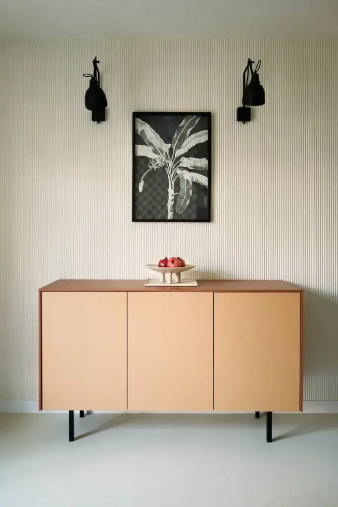 Sideboard in Apricot vor gerillter Wand mit Palmengrafik und schwarzen Leuchten in der Villa Haag