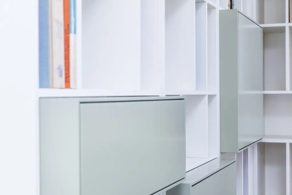 Salbeigrün lackierte Klappen zwischen weißen Regalfächern des Regalsystems H im Detail