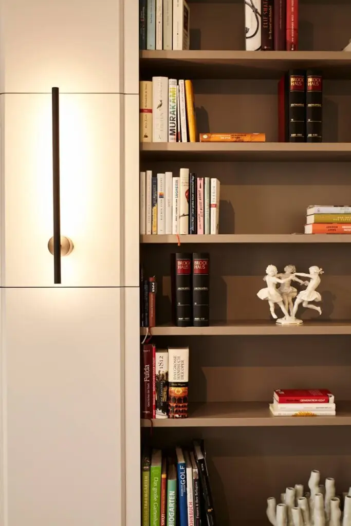 Bücherregal mit Porzellanfiguren neben weißem Schrank mit Lichtleiste in der Villa A
