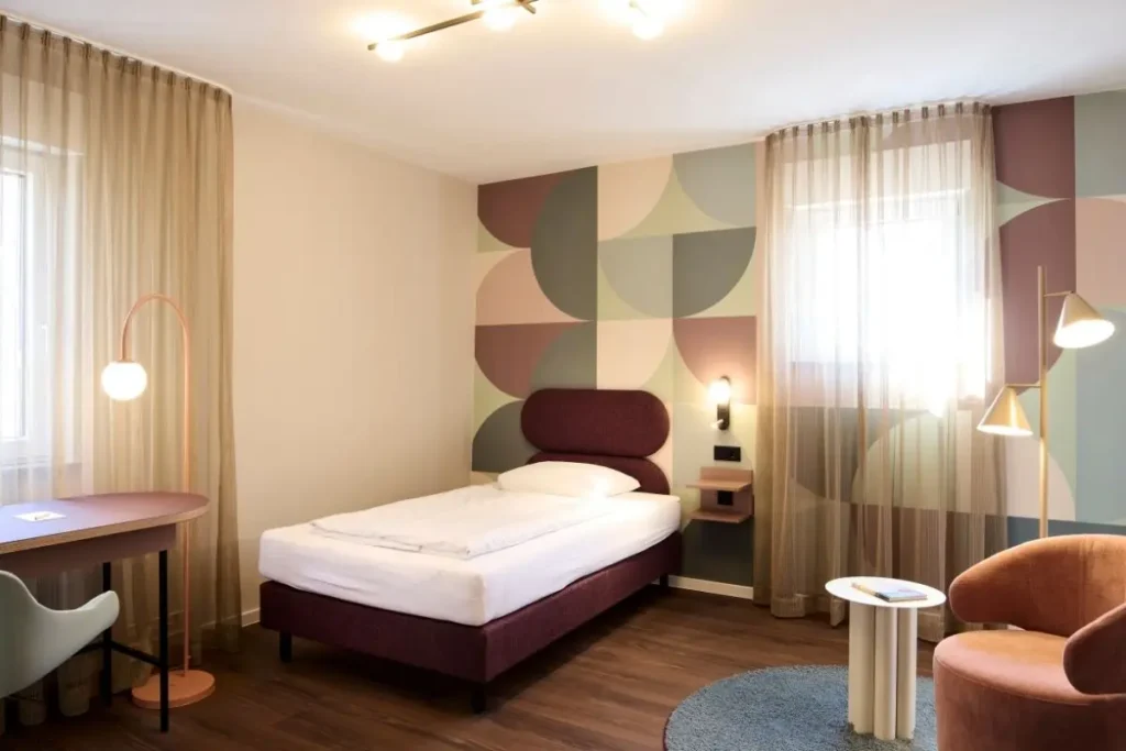 Helles Gästezimmer mit maßgefertigtem Schreibtisch, Bett und rosa Sessel im Gästehaus II des Haus der Standesbeamten